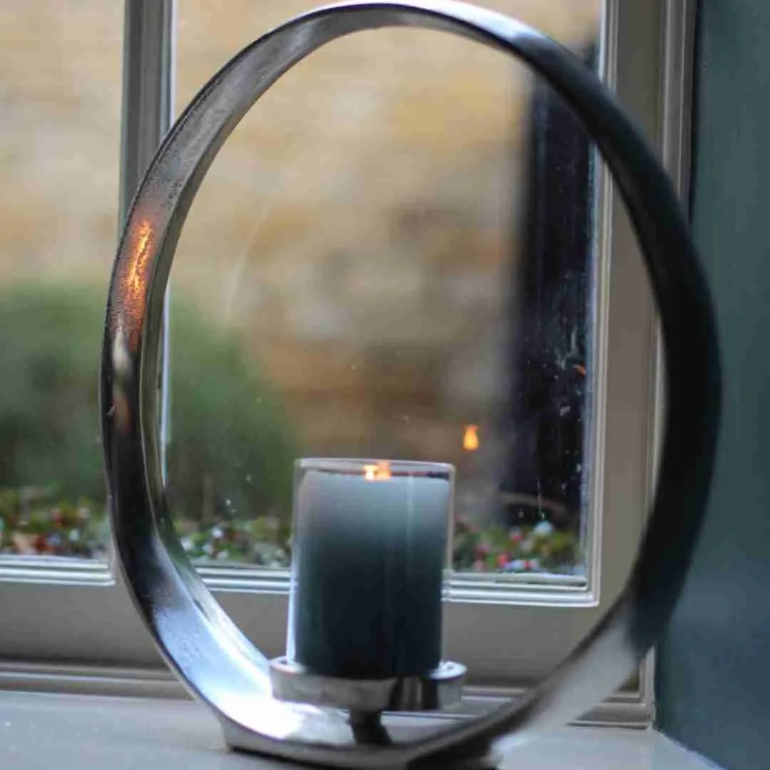 Silver circular candle holder with a glass sleeve in front of a window