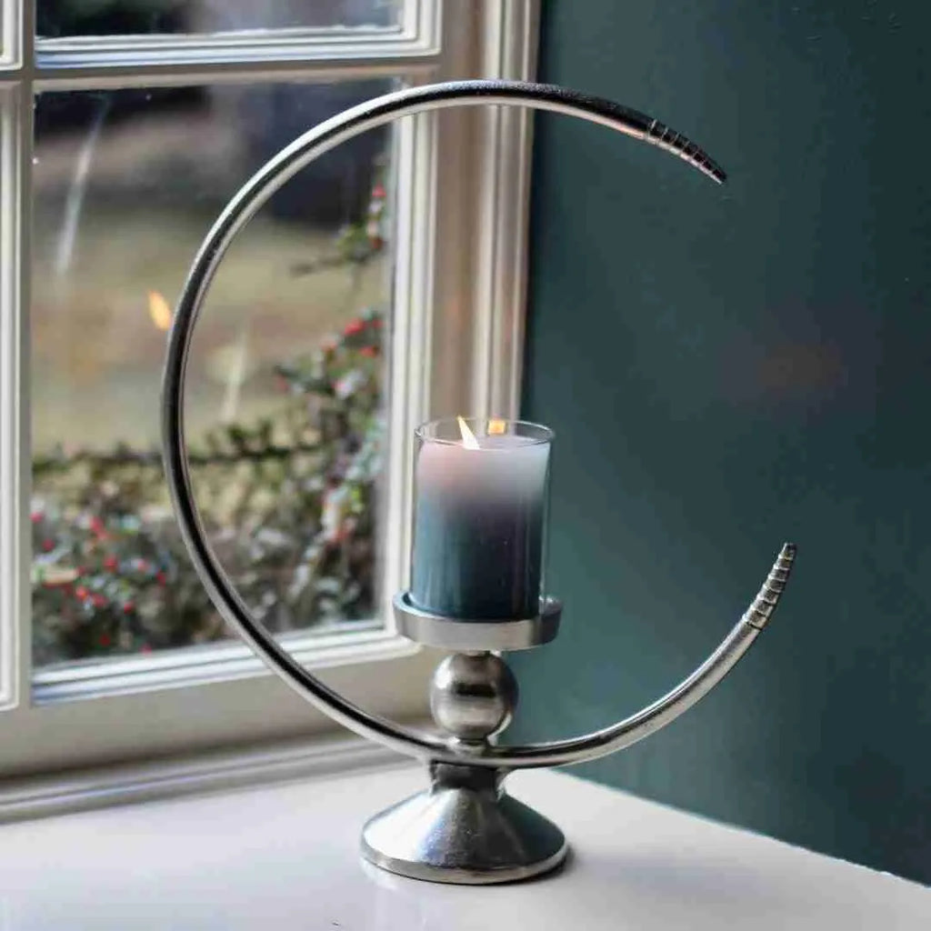 Half moon candle holder in polished metal with a grey pillar candle by a window