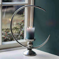 Half moon candle holder in polished metal with a grey pillar candle by a window