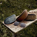 Embossed sunglass cases in turquoise, tan and leopard print on a garden bench