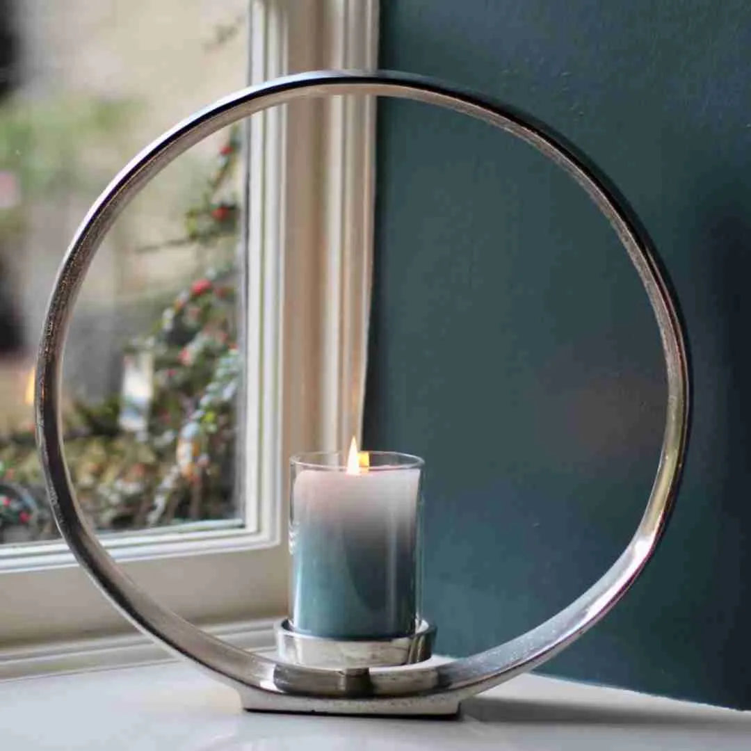 Silver circular candle holder with a lit candle on a windowsill