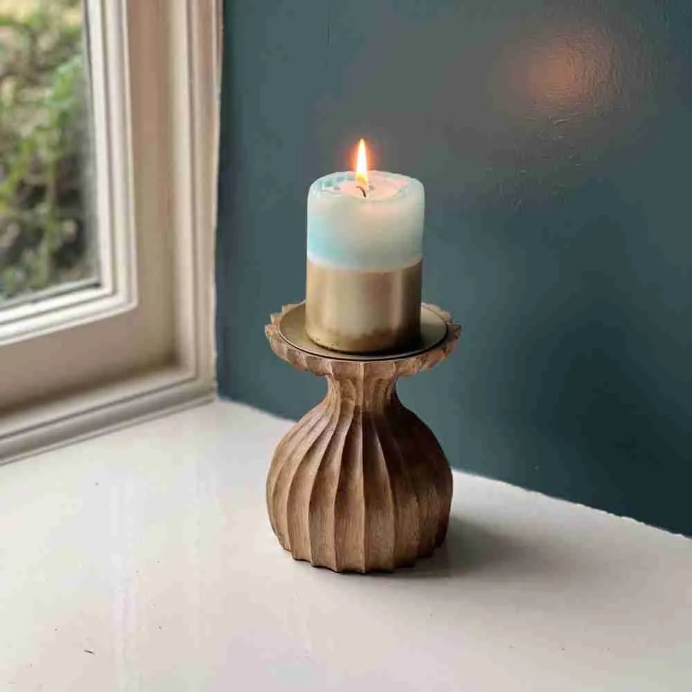 Ribbed wooden candle holder with a lit pillar candle on a windowsill