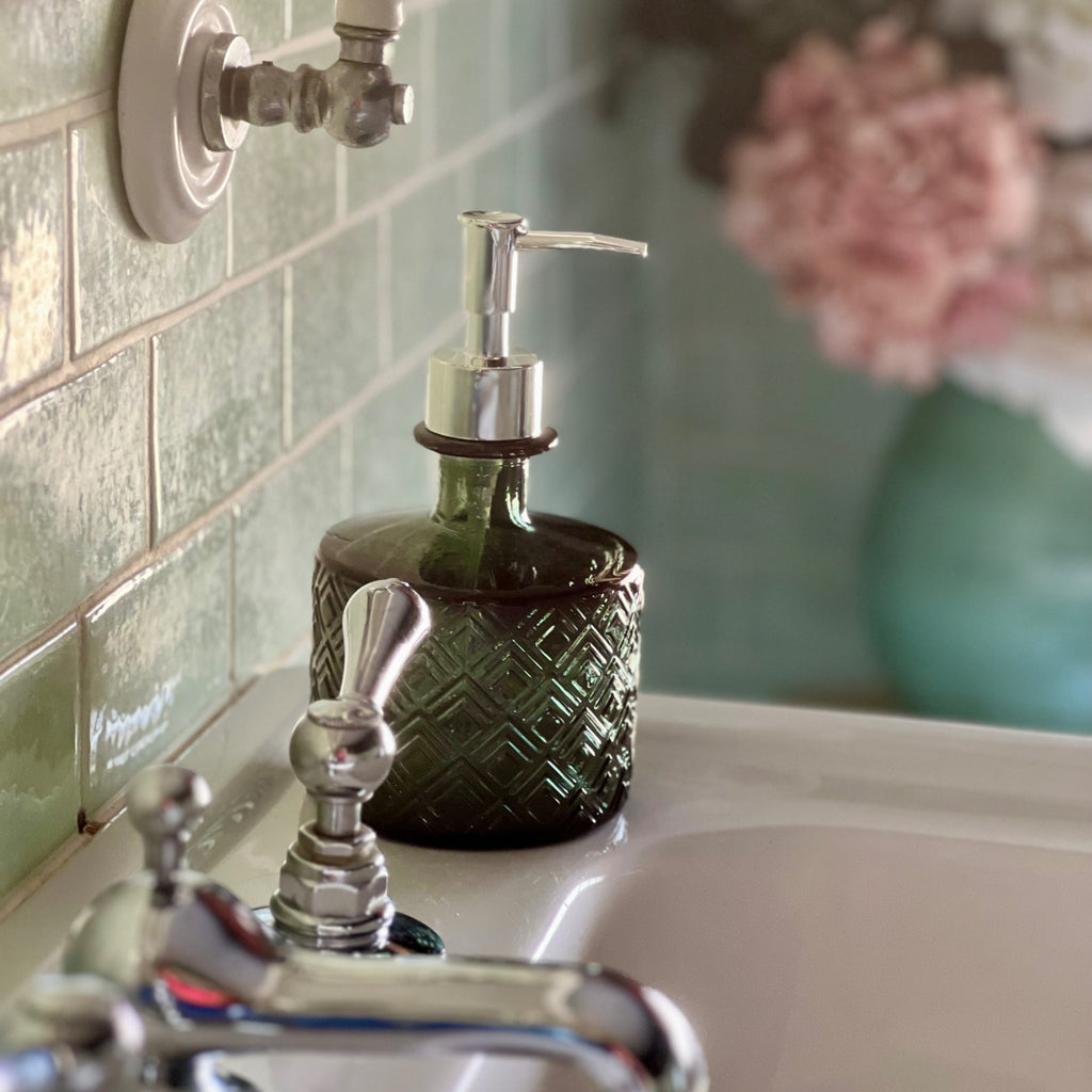Green recycled glass soap dispenser beside a bathroom tap