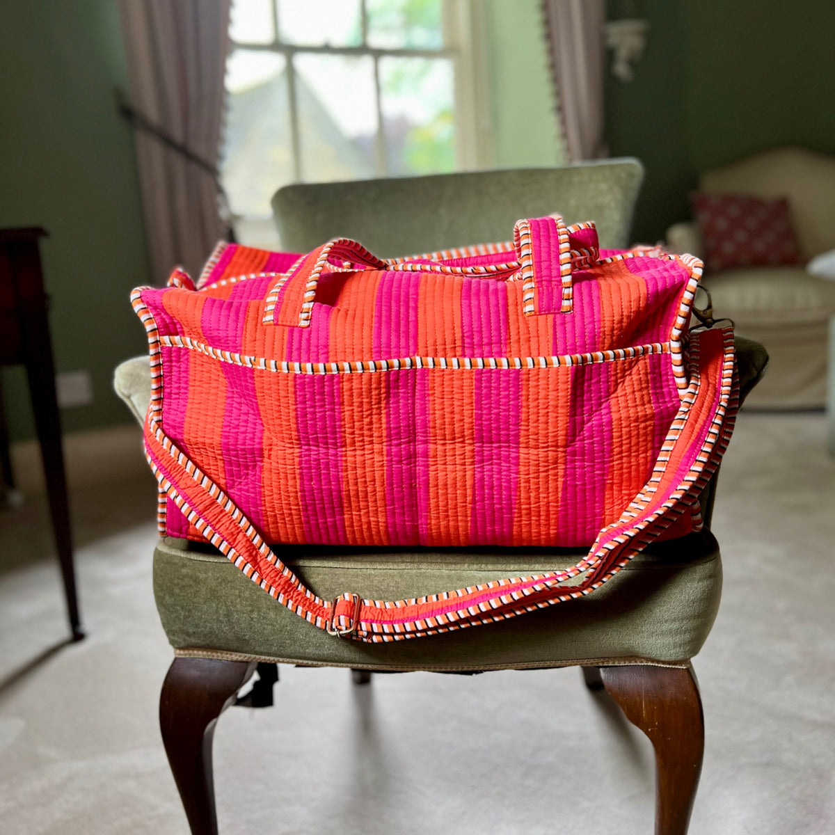 Harlequin quilted cotton weekend bag in orange and pink stripes on a chair