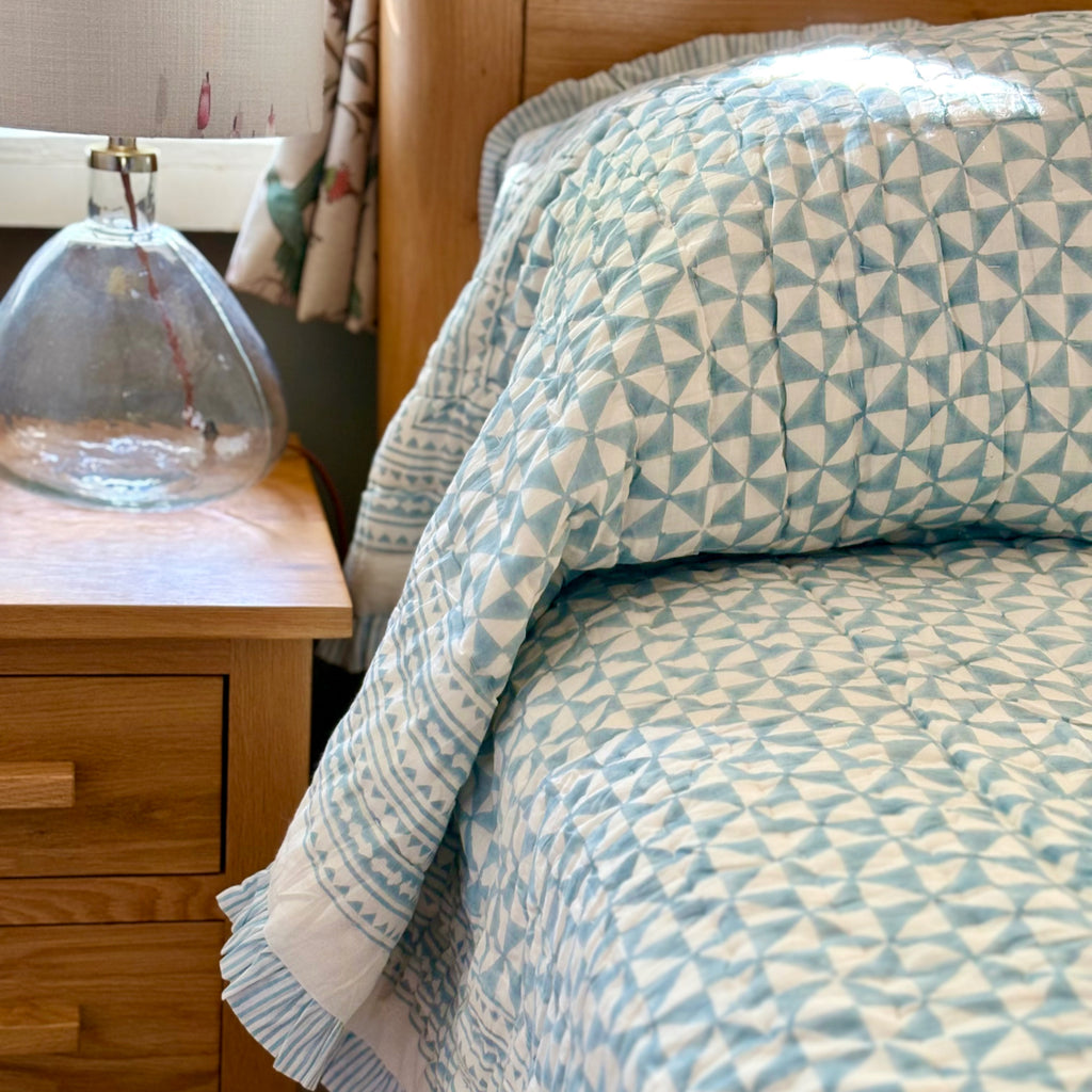 Harlequin reversible cotton quilt in Sea Breeze Blue folded at the foot of a bed