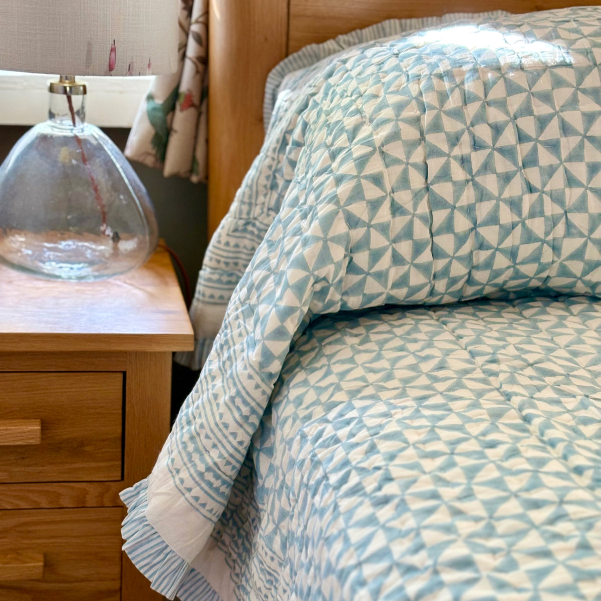 Harlequin reversible cotton quilt in Sea Breeze Blue folded at the foot of a bed