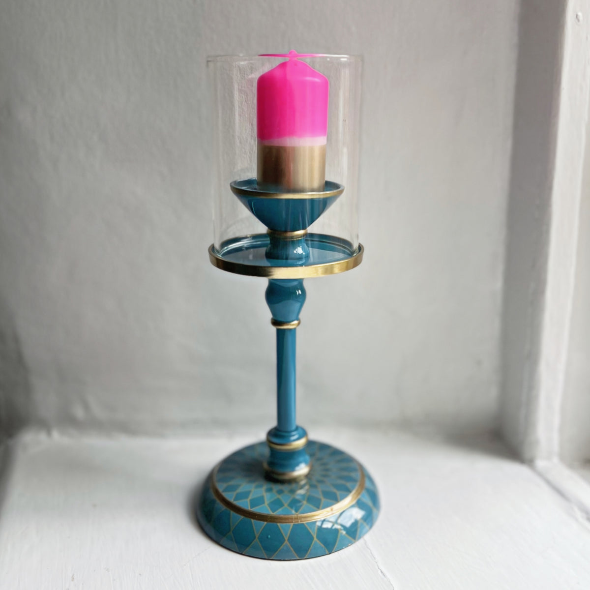 Small gold dipped pillar candle in bright pink, shown in an enamel hurricane candlestick