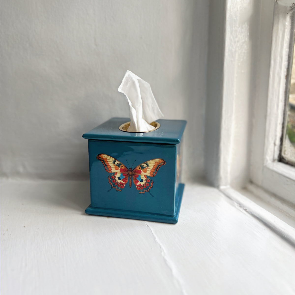 Butterfly square tissue box in teal enamel and brass on a windowsill
