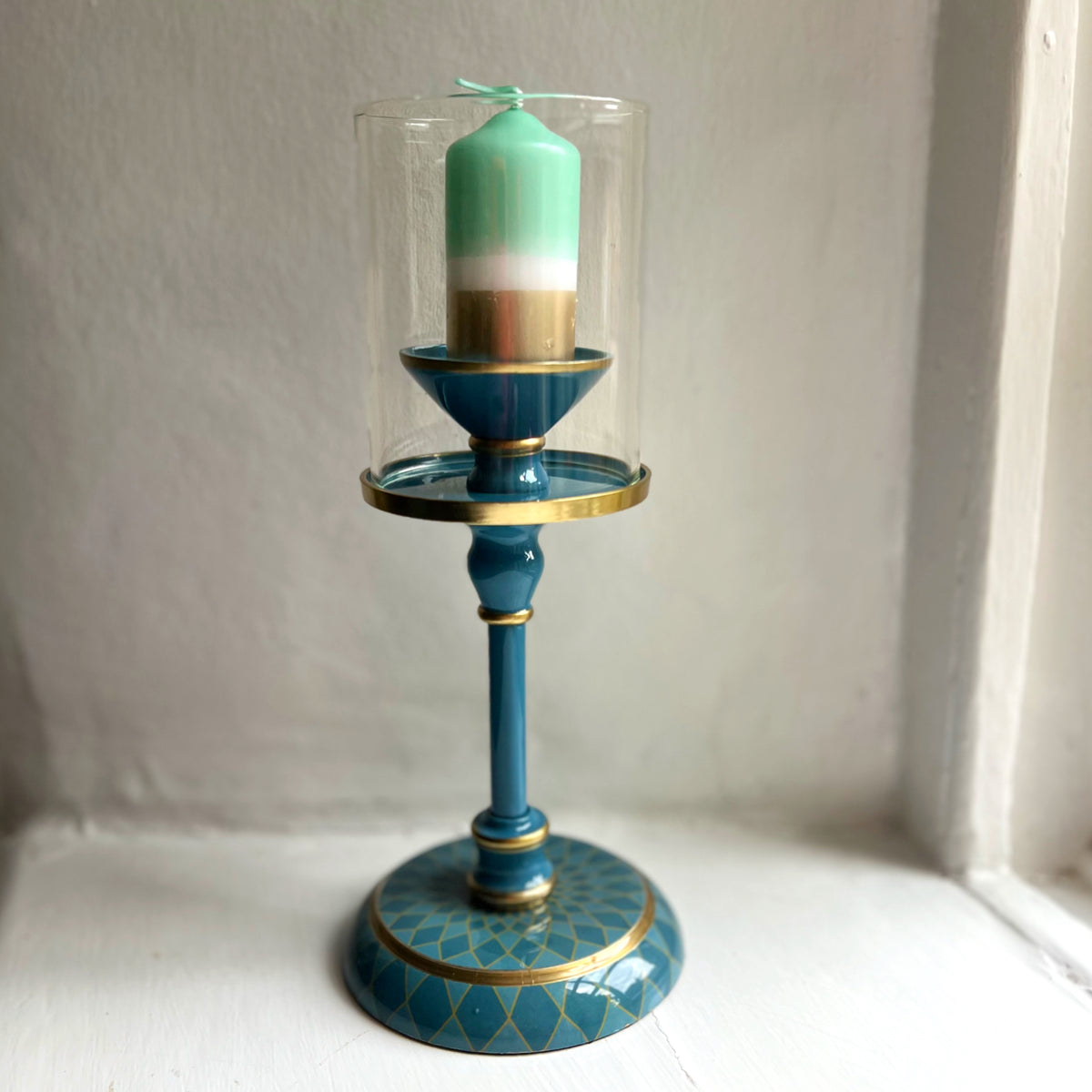 Harlequin hand-enamelled brass hurricane candle holder in Denim Blue with a green pillar candle
