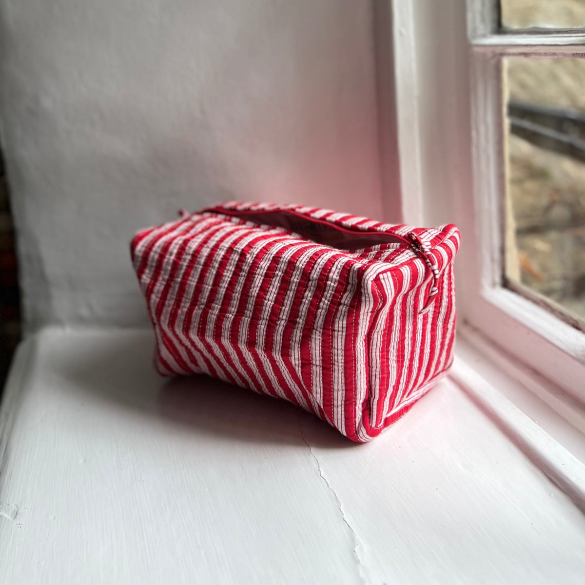 Harlequin quilted cotton washbag in red stripe on a windowsill