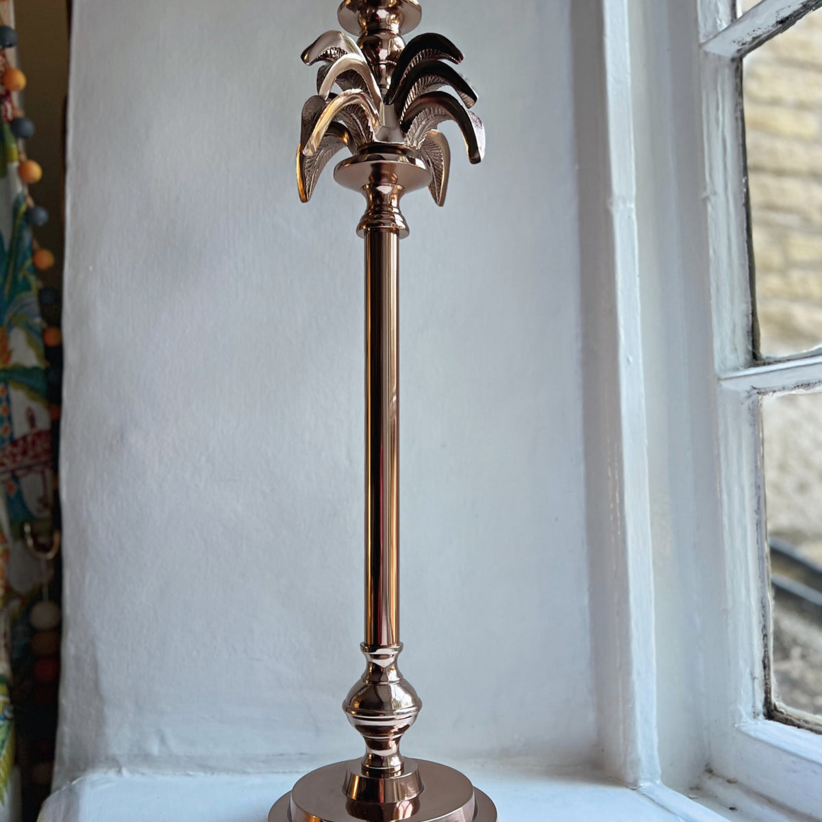 Large palm tree candlestick in rose gold on a windowsill