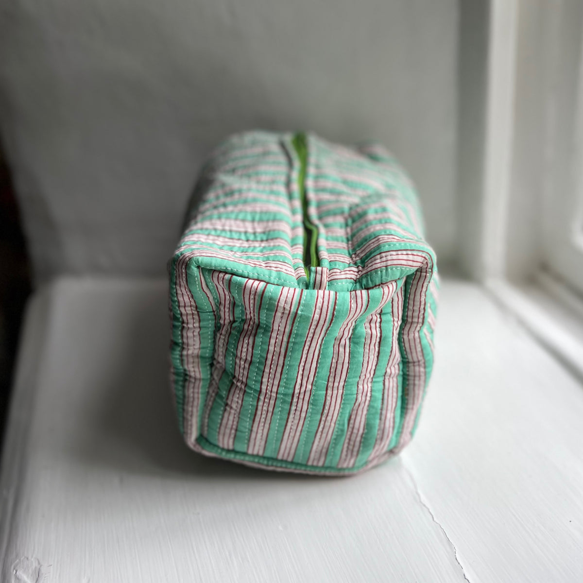 Harlequin quilted cotton washbag in green stripe on a windowsill