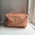 Harlequin quilted cotton washbag in orange stripe on a windowsill