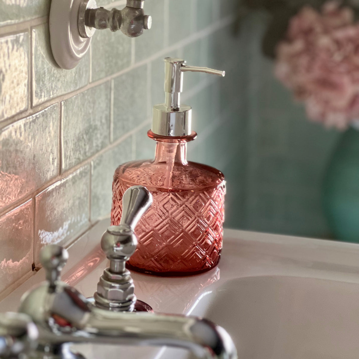 Pink recycled glass soap dispenser beside a bathroom tap