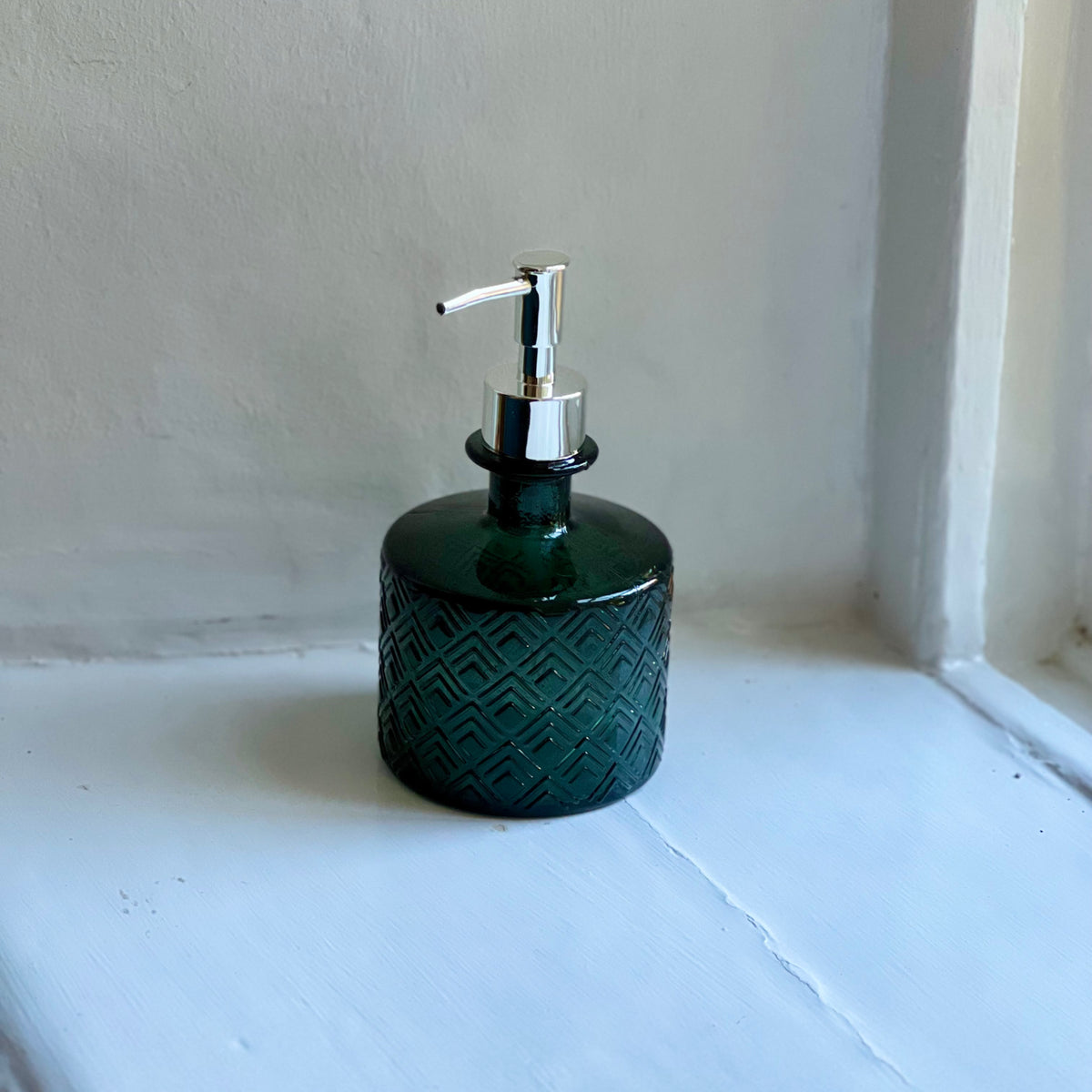 Green recycled glass soap dispenser on a windowsill