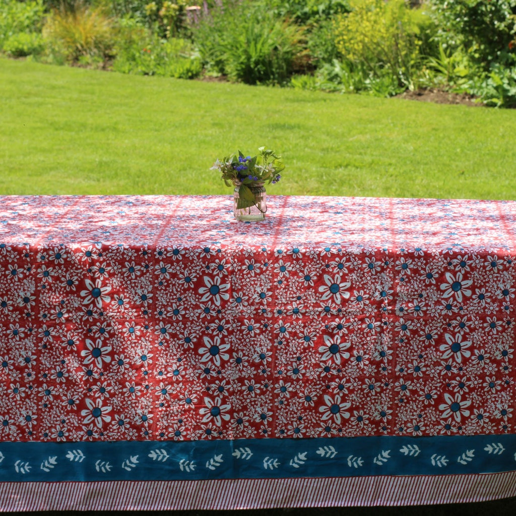 Red daisies rectangular tablecloth with a blue border on a garden table