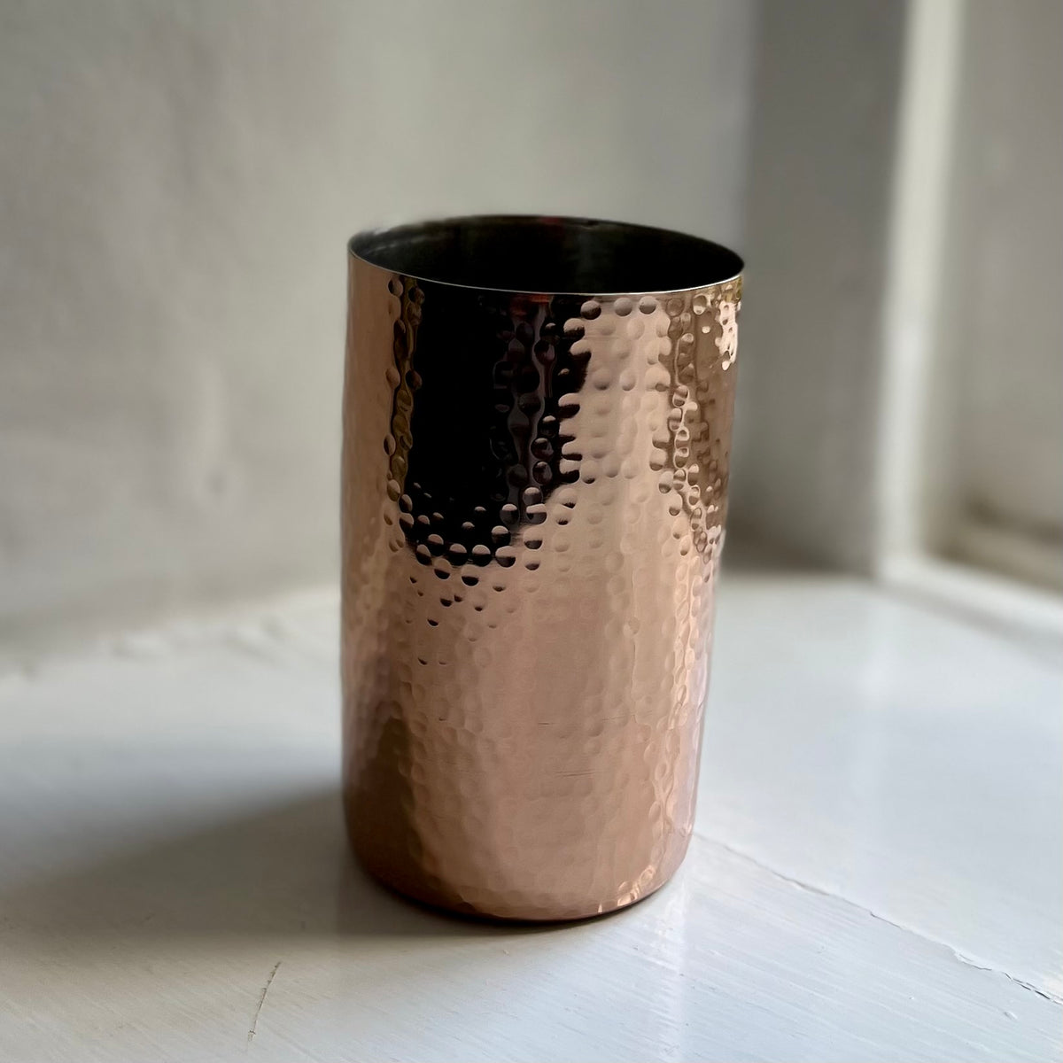 Handmade hammered metal tumbler in rose gold on a windowsill