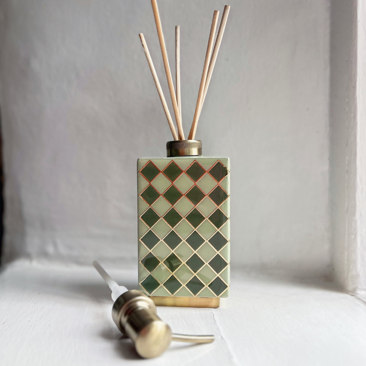 Harlequin enamel and brass multi-use bottle in Sage Green used as a reed diffuser