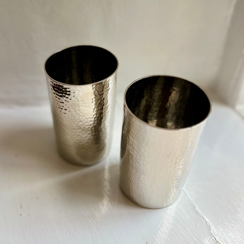 Two silver hammered metal tumblers on a windowsill