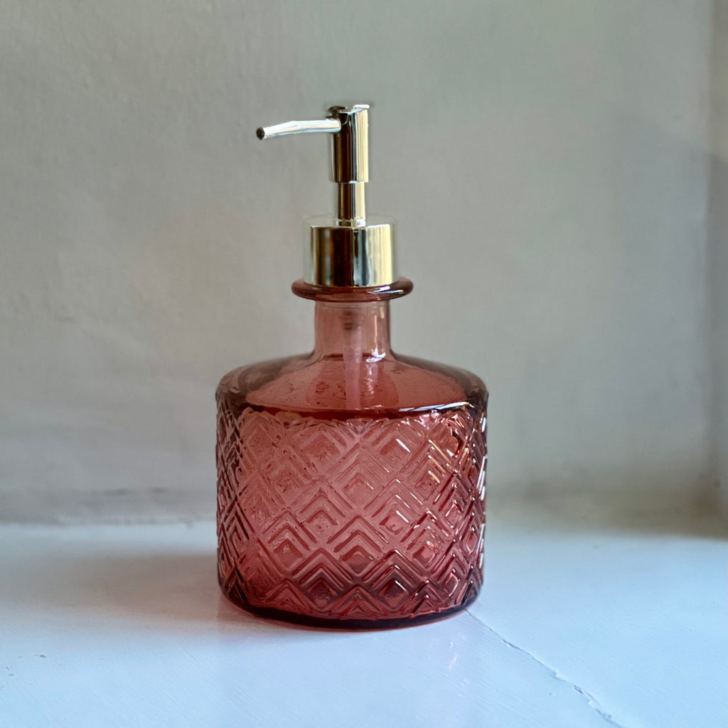 Pink recycled glass soap dispenser on a white shelf