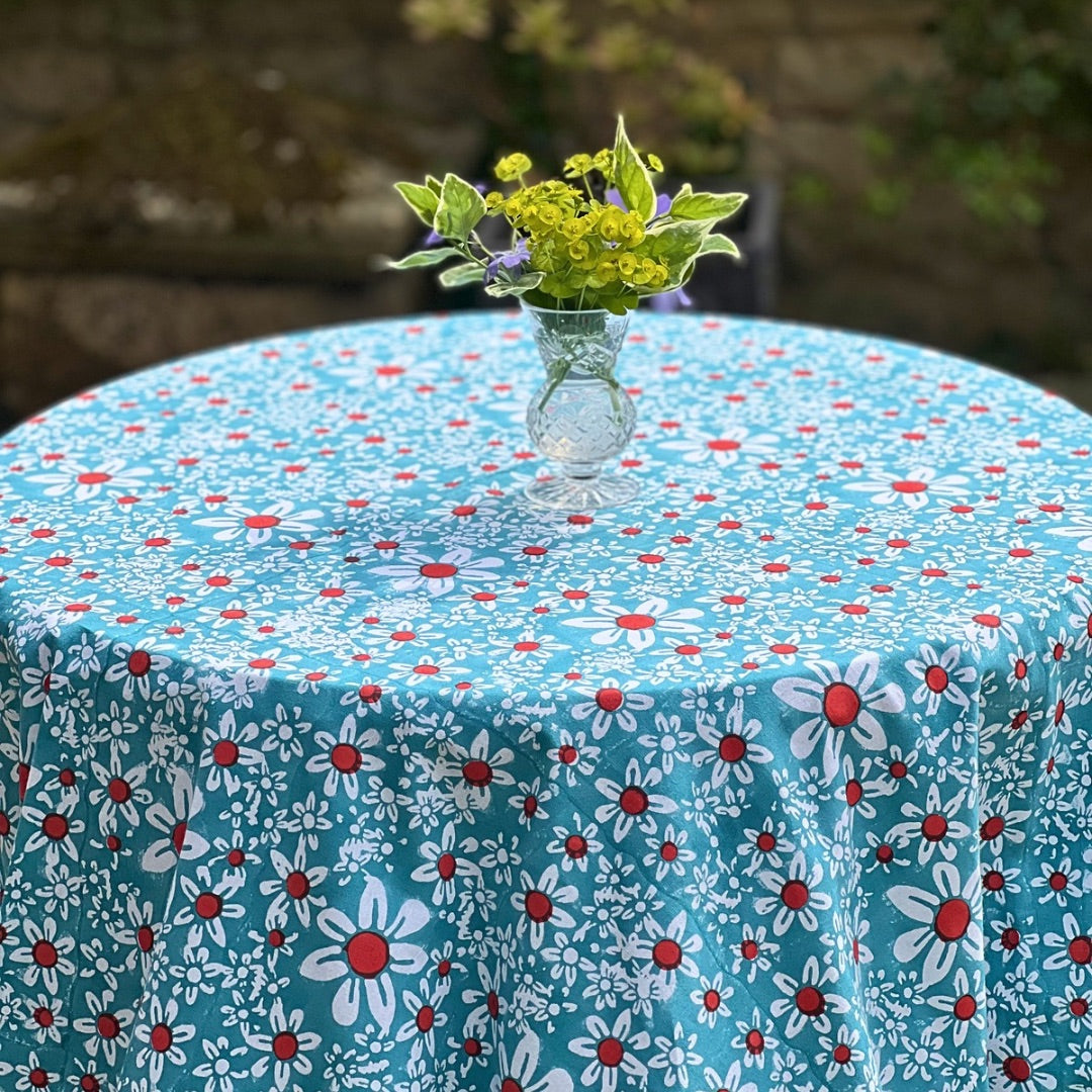 Round turquoise daisies tablecloth on a garden table with a vase of flowers