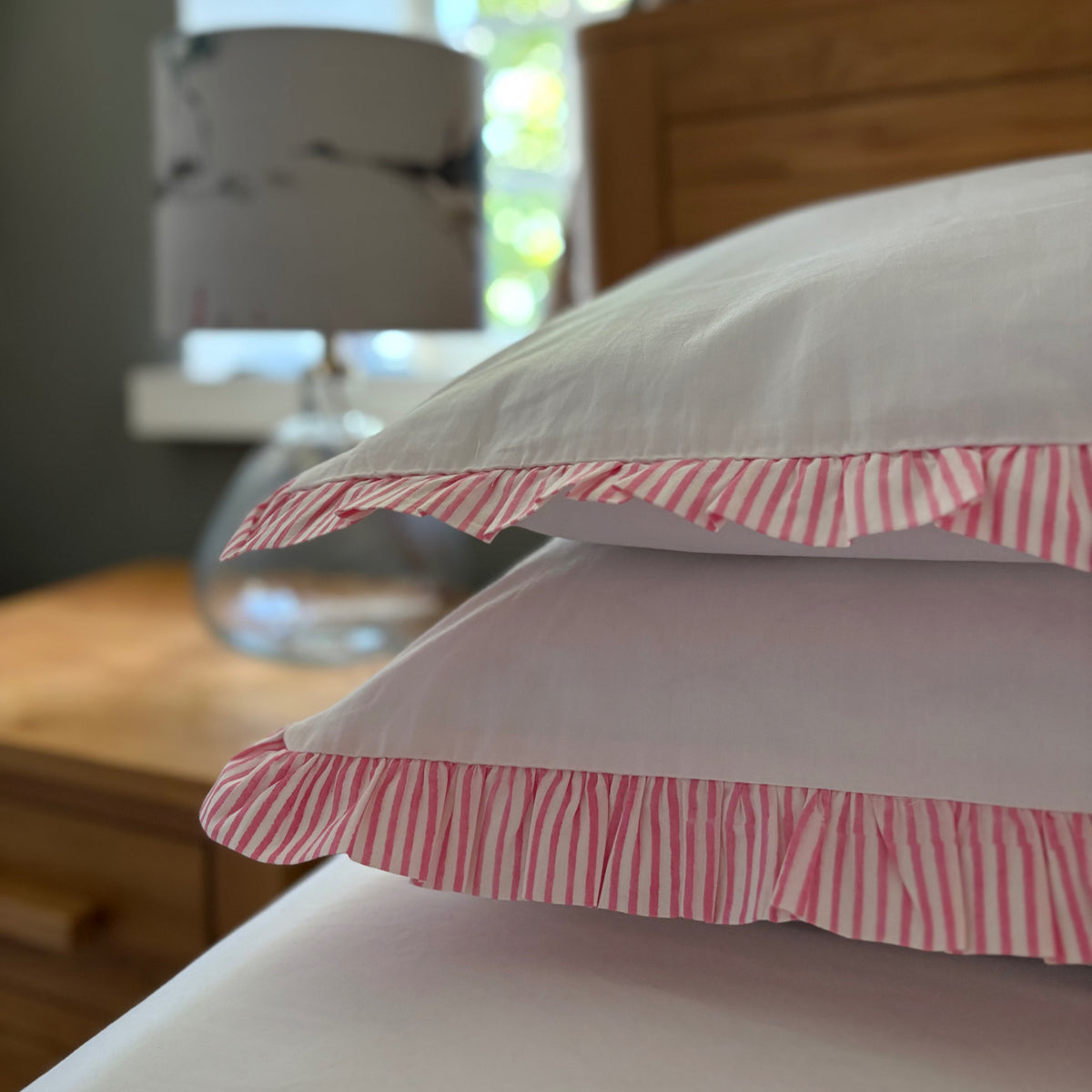 Pair of Harlequin cotton pillowcases with Raspberry Pink striped frills on a bed