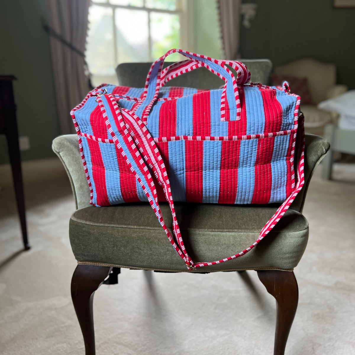 Harlequin quilted cotton weekend bag in red and blue stripes on a chair