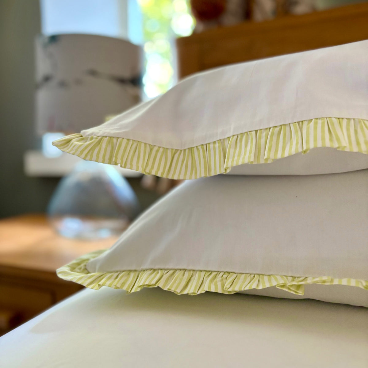 Pair of Harlequin cotton pillowcases with Apple Green striped frills on a bed