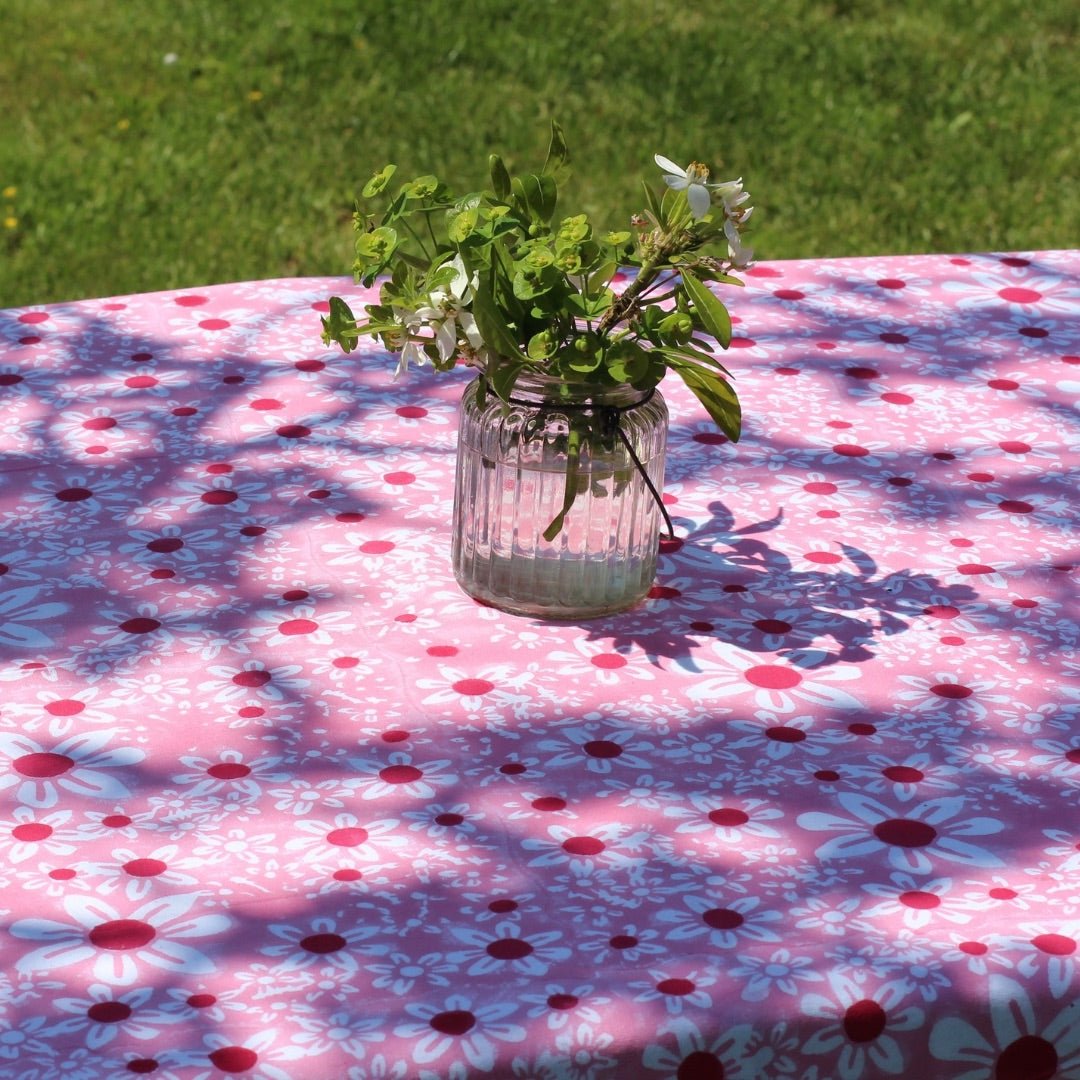 Pink daisies tablecloth in dappled sunlight with a glass vase