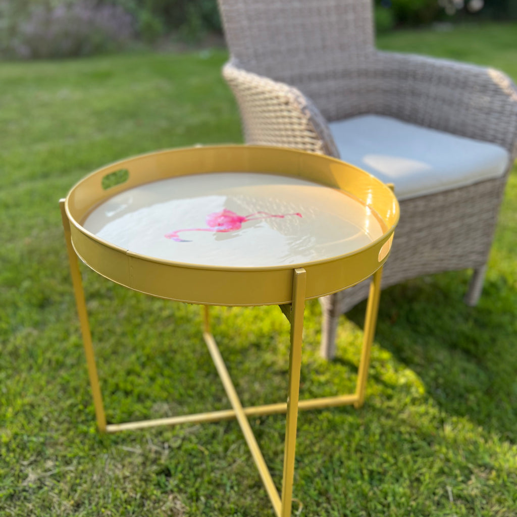 Gold ottoman tray stand with a round tray beside a garden chair